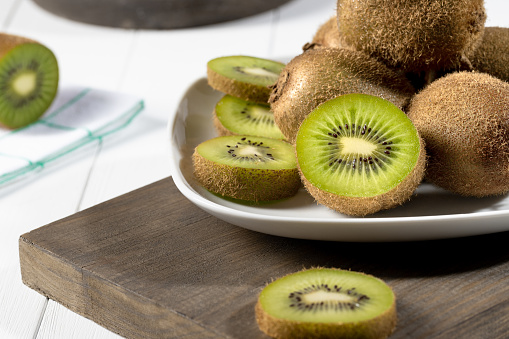 Close up fresh kiwi and slices on white plate on white wooden background. Selective focus.