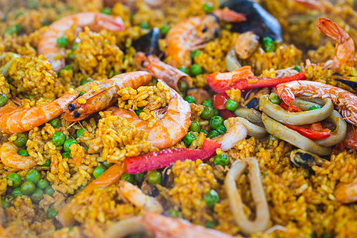 Close up image showing a delicious paella made up of bright coloured yellow rice, mussels in their shells, slices of lemon, prawns and peas. Lots of room for copy space.