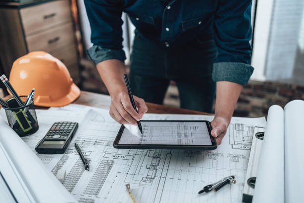 istock Engineering working with drawings inspection on tablet in the office and Calculator, triangle ruler, safety glasses, compass, vernier caliper on Blueprint. Engineer, Architect, Industry and factory concept. 1458800332