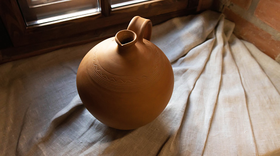 Ancient pottery stands on the window sill. Brown earthenware jug. Pottery, close-up