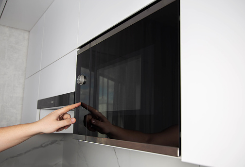 A man presses his finger on the touch panel of a microwave oven to turn on the defrost function. High tech modern microwave oven, functions. Copy space for text