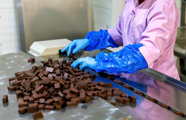 primer plano de las manos de una trabajadora clasifica la producción de la línea de dulces de chocolate en la fábrica - food industry manufacturing human hand fotografías e imágenes de stock