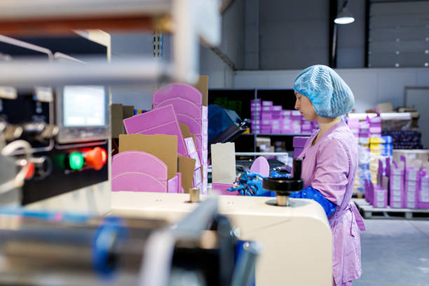 istock Professional female worker in uniform and protective gloves packed chocolate candies in boxes on production line at factory 1458801581