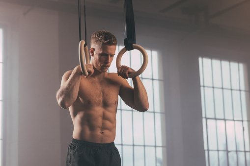 A handsome Caucasian athlete doing his daily workout in the gym using still rings.