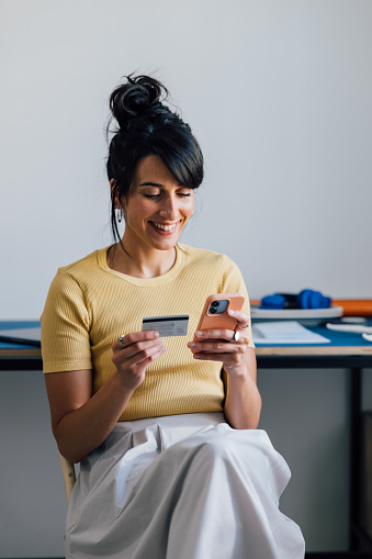 A smiling Caucasian entrepreneur transferring money using an app on her mobile phone.