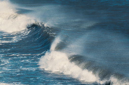 Powerful blue ocean wave with splashing hitting on black sand beach in summer