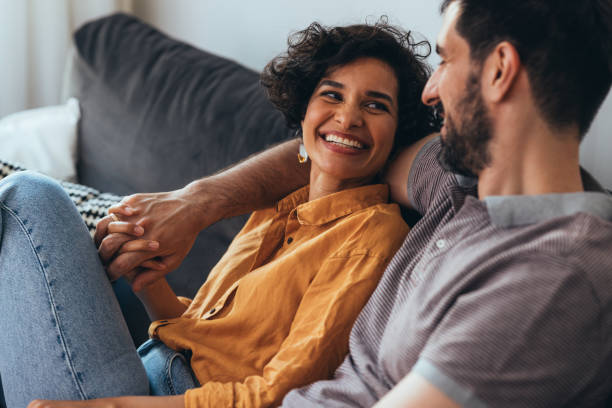 A Happy Beautiful Couple Sitting On The Cozy Sofa At Home And Relaxing A smiling Latin-American woman and her Caucasian boyfriend enjoying spending their leisure time together. lifestyle couple stock pictures, royalty-free photos & images