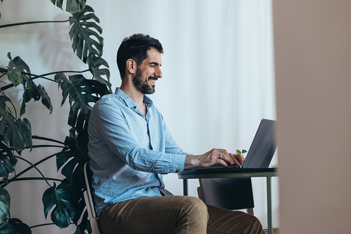 A smiling handsome Caucasian entrepreneur typing on his computer.