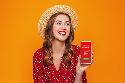 girl holding mobile phone and doing online shopping isolated on orange background in studio