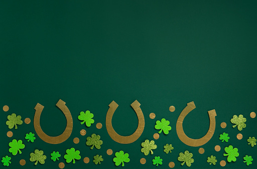 St. Patrick's Day celebration Concept. Greeting card with traditional symbols - Golden horseshoes, gold coins and clover leaves, green shamrocks on green background. Top view, copy space.