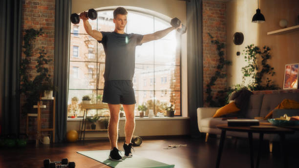 istock Fit Athletic Strong Young Man Doing Core Strengthening Workout with Dumbbells During Morning Session at Home in Sunny Apartment. Concept of Healthy Lifestyle and Fitness. 1458813514
