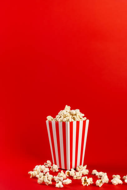 istock Popcorn in a red and white striped bag on a red background. Front view, copy space 1458813705