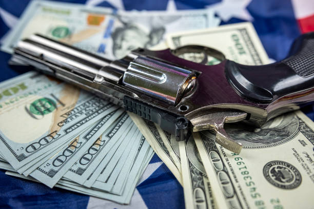 vue de dessus d’un gros pistolet noir et d’un tas de dollars américains sur un grand drapeau américain spacieux. - currency crime gun conflict photos et images de collection