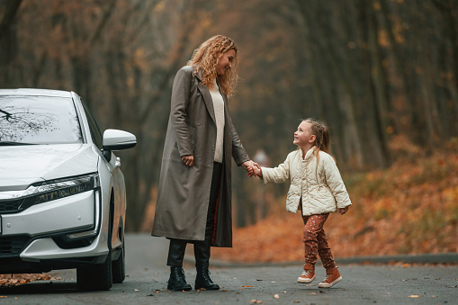 Mother with her daughter is outdoors near electric car outdoors.