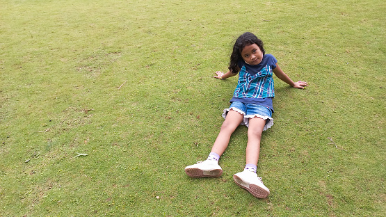 Little girl sitting facing camera in meadow on sunny day