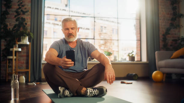 istock Portrait of a Strong Athletic Fit Senior Man Using Smartphone in Between Workouts During Morning Exercises at Home in Sunny Apartment. Healthy Lifestyle, Fitness, Recreation, Wellbeing and Retirement. 1458815966