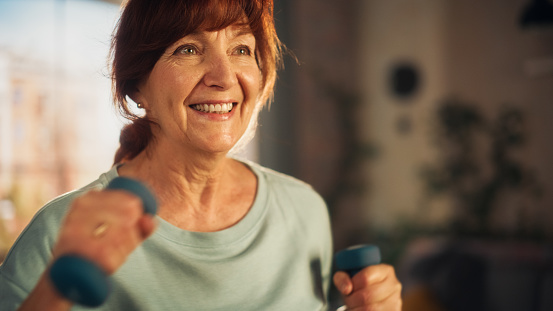 Portrait of a Senior Woman Exercising and Training at Home on Sunny Morning. Elderly Female Strengthening Arm Muscles with Dumbbell Workout in Loft Apartment Living Room. Wellness and Fitness.