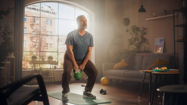 istock Strong Athletic Fit Middle Aged Man Lifting and Swinging a Heavy Kettlebell, Doing Core Strengthening Exercises During Morning Home Workout in Cozy Apartment. Concept of Fitness Lifestyle. 1458816384