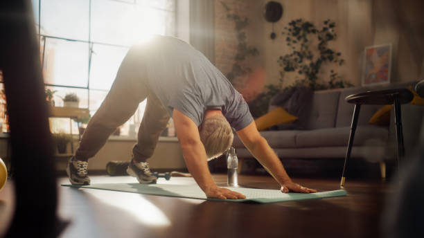 istock Strong Athletic Fit Middle Aged Man Training on a Yoga Mat, Doing Back Stretching and Core Strengthening Exercises During Morning Workout at Home in Sunny Apartment. Concept of Health and Fitness. 1458816604