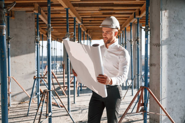 In shirt and black pants. Reading the plan. Man is working on the construction site at daytime stock photo