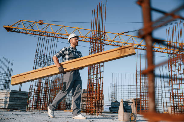 istock View from the side. Walking and holding wooden plank. Man is working on the construction site at daytime 1458818022