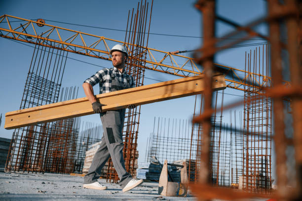 istock View from the side. Walking and holding wooden plank. Man is working on the construction site at daytime 1458818028