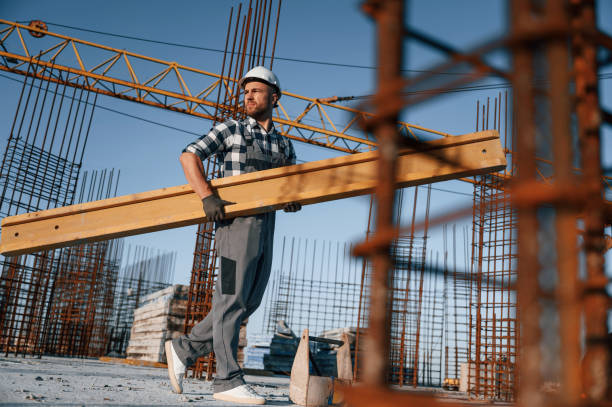 istock View from the side. Walking and holding wooden plank. Man is working on the construction site at daytime 1458818045