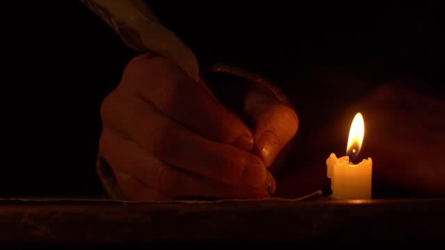 Hand writing with a quill pen by a candle