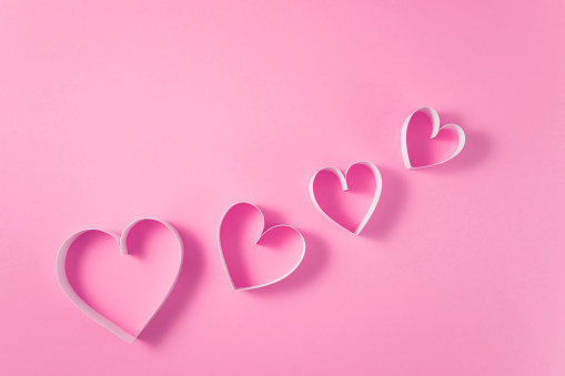 Heart shaped papers on pink background with copy space