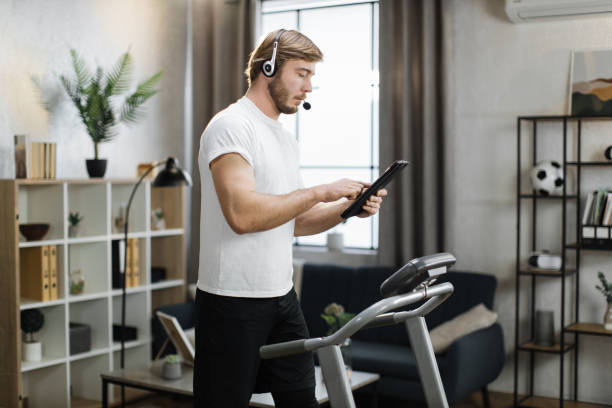 kaukaski mężczyzna w sportowym ubraniu za pomocą zestawu słuchawkowego działającego tabletu podczas treningu cardio - businessman exercising training muscular build zdjęcia i obrazy z banku zdjęć