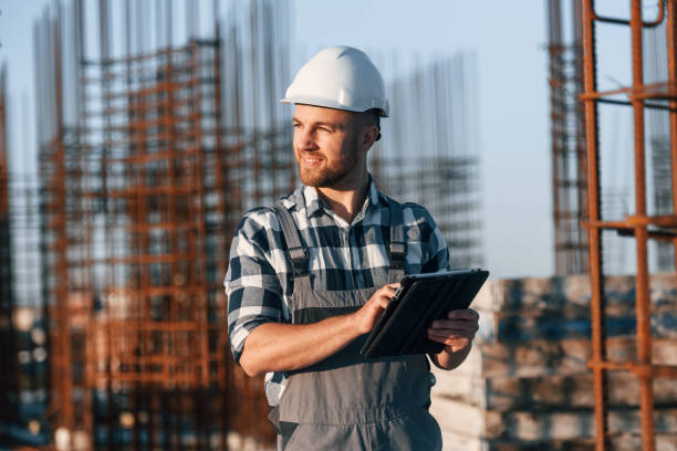 istock Looking to the side. Holding tablet. Man is working on the construction site at daytime 1458820998