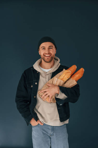 istock Holding baguettes. Handsome man is in the studio against blue background 1458824711