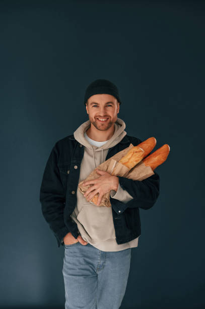 istock Holding baguettes. Handsome man is in the studio against blue background 1458824716