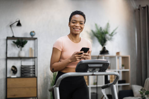 istock Close up view of young sporty african woman using running machine simulator while making selfie 1458825586