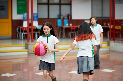 Front view of smiling elementary age girl in uniform holding ball and exercising with friends.