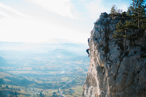 Two climbers on ferrata trail climbing the mountain. Mountaineers rock climbing a face of a cliff.