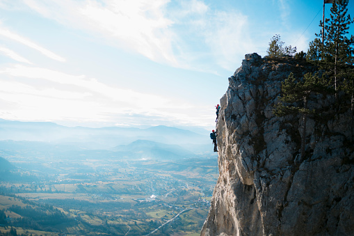 Two mountaineers rock climbing a face of a cliff. Two people climbing the mountain on ferrata trail.