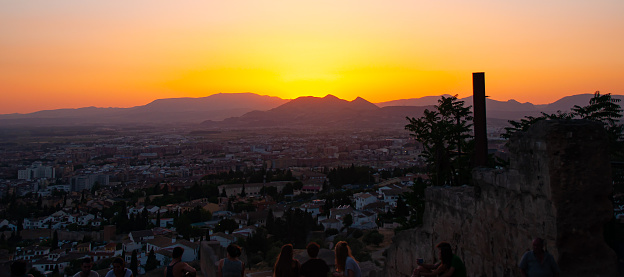 A group of tourists watches the beautiful sunset on a hill over the mountain range in Granada, Spain