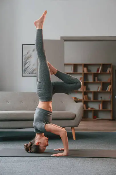 Making headstand. Young woman in yoga clothes doing fitness indoors.