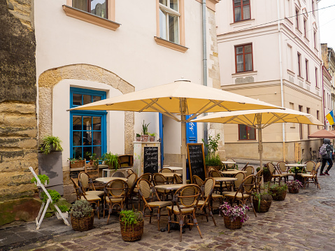 Lviv, Ukraine- July, 2022: Cozy outdoor cafe in the old town of Lviv. Summer cafe with umbrellas in the narrow old street. Vintage tables on paved street among flower pots.
