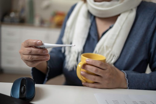 Cropped shot of an adult woman checking her temperature on a digital thermometer