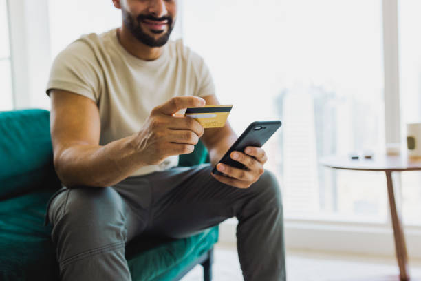 Close-up of bearded man shopping with cellphone and holding credit card on couch stock photo