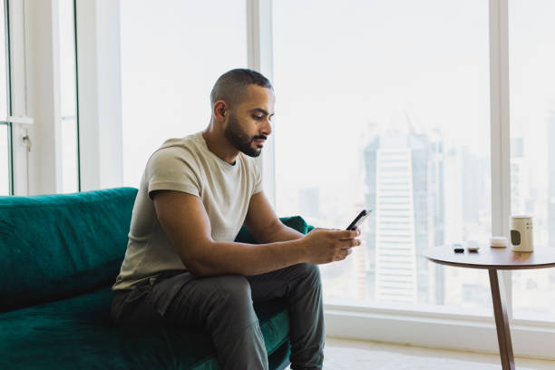 istock Bearded man using cellphone on couch in modern apartment 1458834450