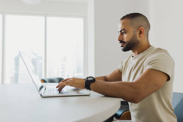 Side view of man with beard busy with work on laptop in home office Man with beard focusing on work with laptop at desk in modern home office crew cut stock pictures, royalty-free photos & images