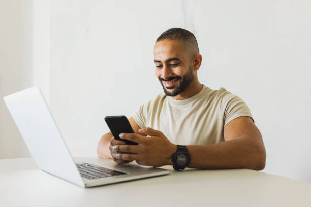 istock Cheerful man with beard using cellphone at desk in home office 1458834527