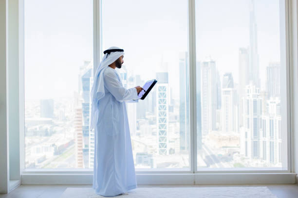 vista lateral de un hombre de negocios árabe usando una tableta digital junto a la ventana en una oficina moderna - agal fotografías e imágenes de stock