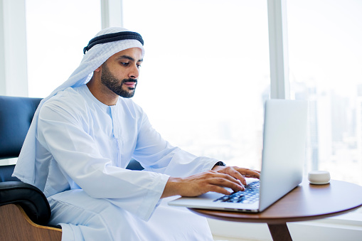 Bearded Arab businessman focused at work and typing on laptop at desk in modern office