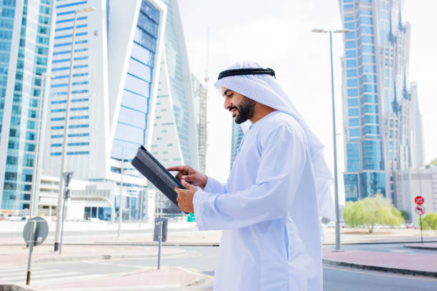istock Side view of cheerful Arab businessman with beard using digital tablet on street 1458836198