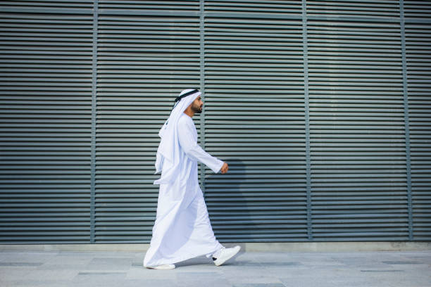 Side view of bearded Arab businessman walking past metal grille stock photo