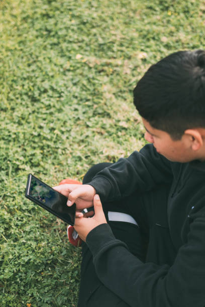 istock top view young boy sitting in the park, looking at his smart phone, selective focus 1458837979